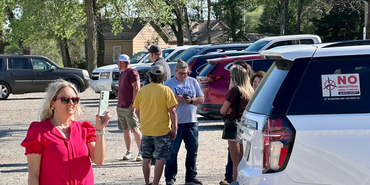 Rice County residents standing in a parking lot after the community meeting was canceled, a No Industrial Wind Turbines sticker on a vehicle window.